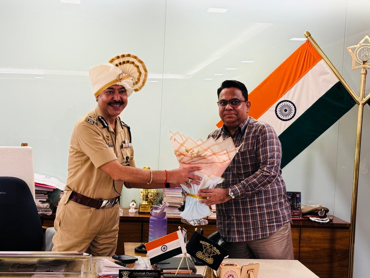Ashutosh Dumbare in uniform, wearing a ceremonial pheta, receiving a bouquet from a visitor at the Thane police commissioner's office.
